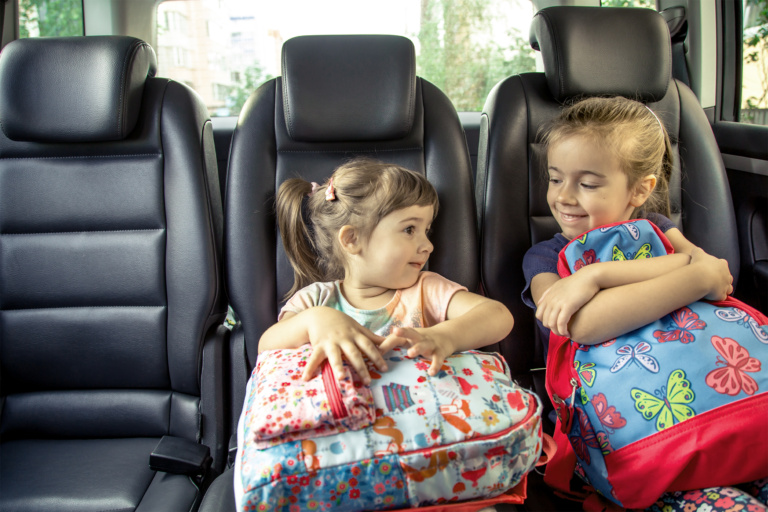 Children in the car go to school, happy, sweet faces of sisters, pupils of a kindergarten with school backpacks, sitting in the parental car